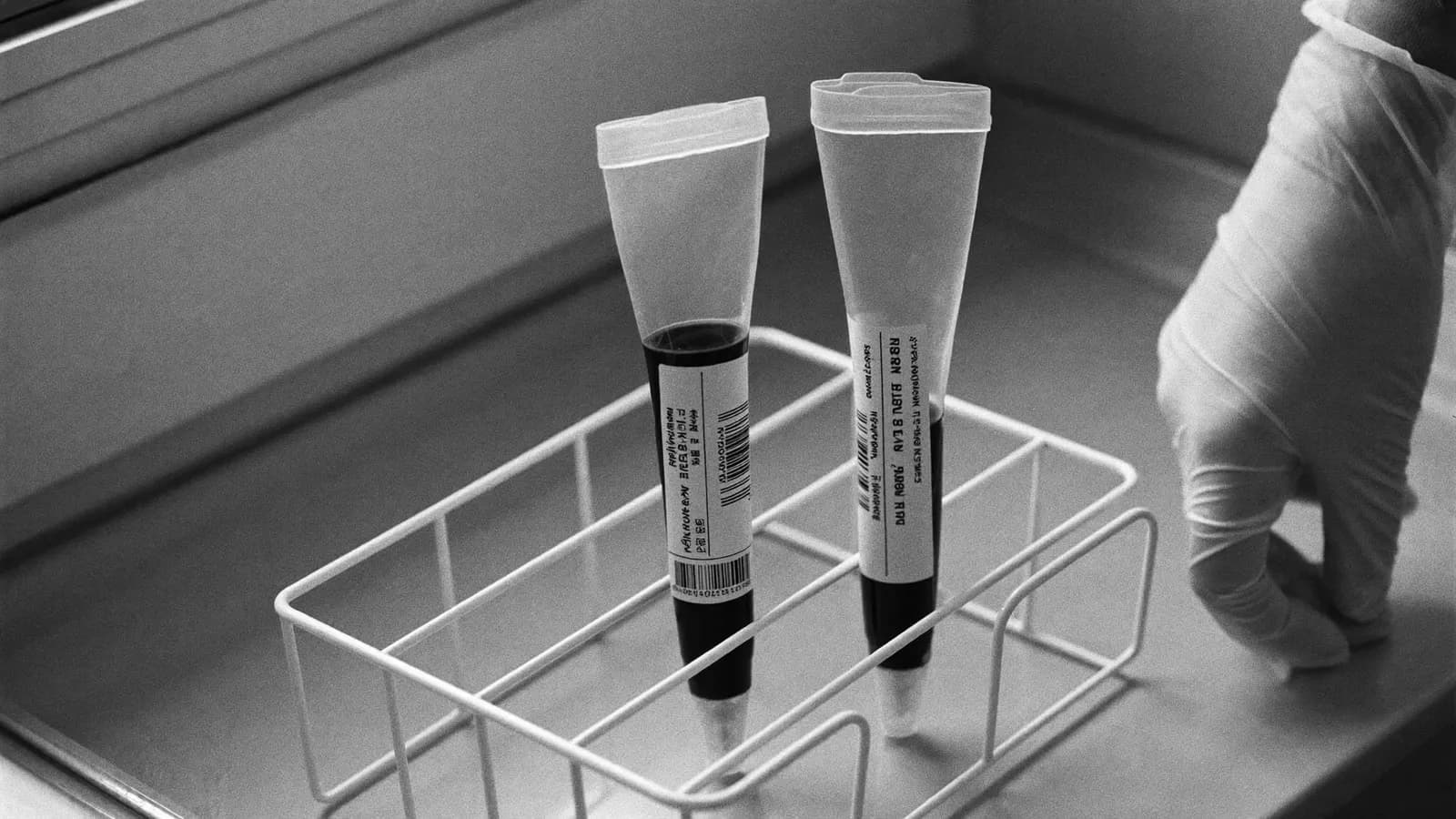 A small laboratory centrifuge with two sealed blood tubes on a white bench
