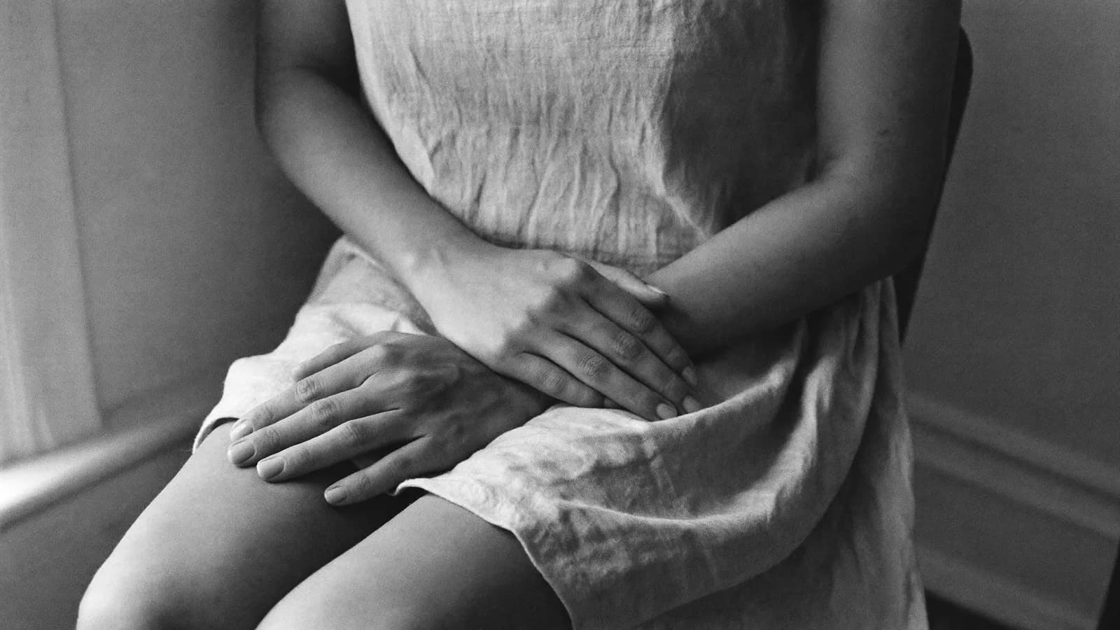 A woman's hands resting in her lap on a linen dress in soft window light